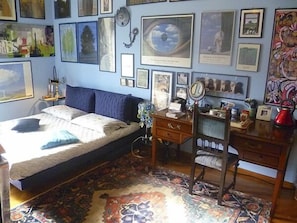 A bedroom with a bed, dresser, desk, and a wall adorned with framed pictures.