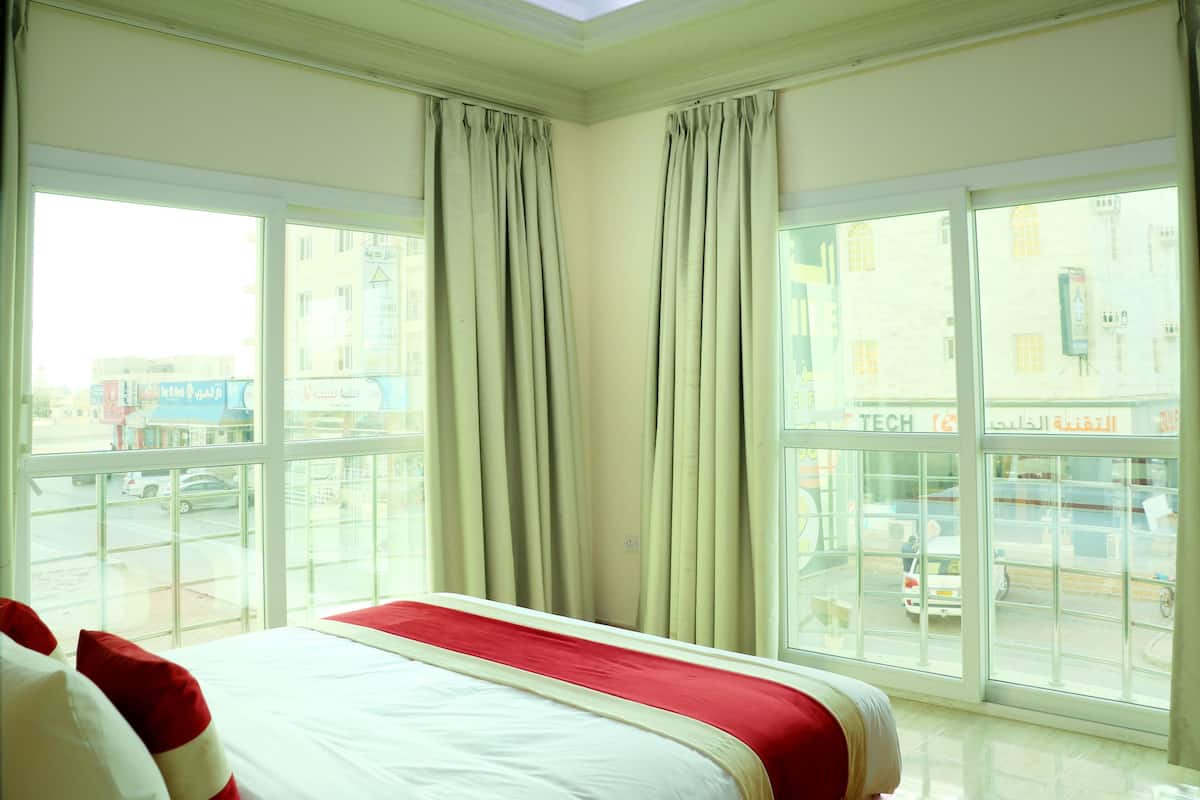 A hotel room with a bed, large windows, and curtains.