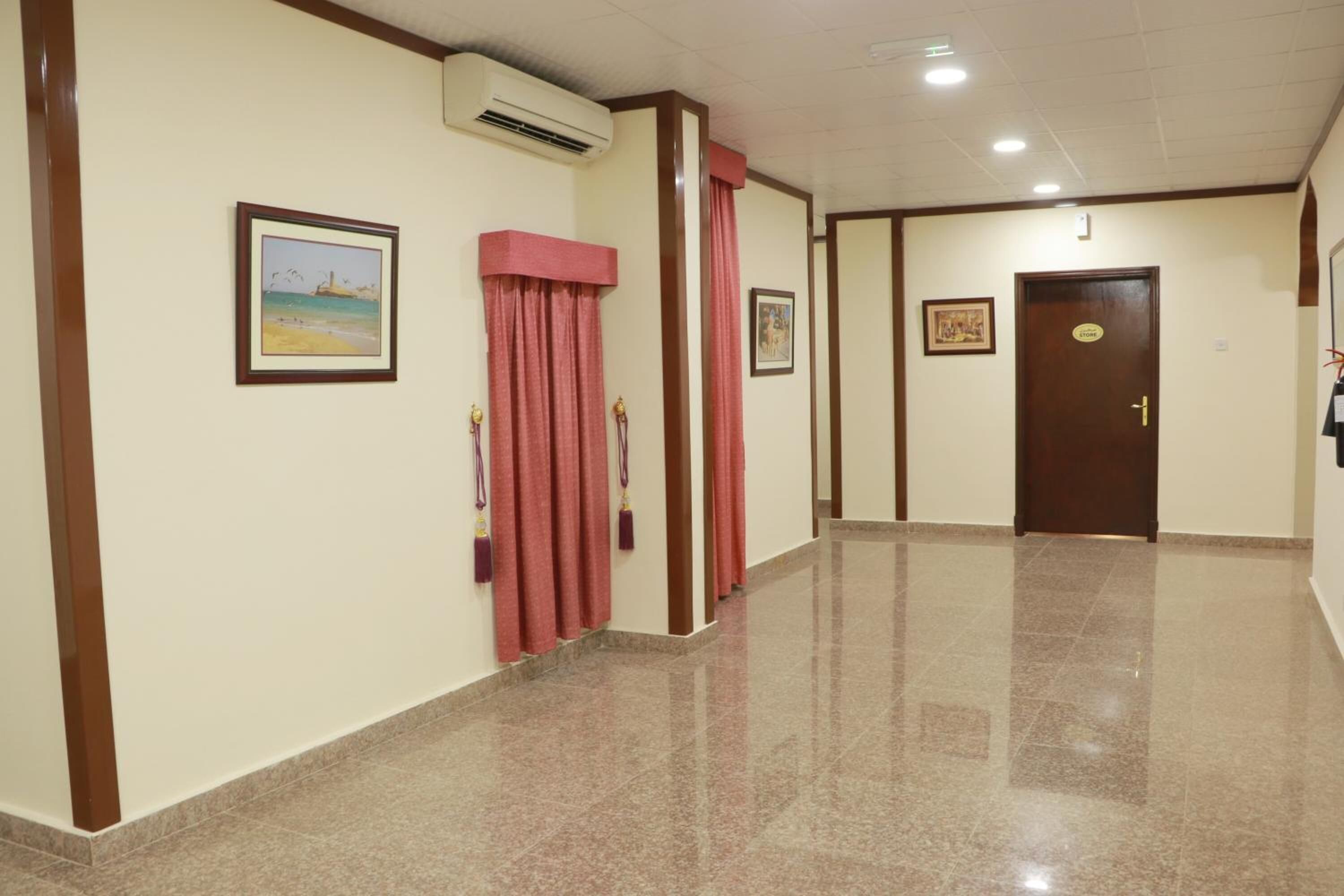 A hallway with a polished floor, framed pictures on the walls, and a door with a sign.
