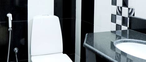 Un baño con inodoro blanco, salpicadero de azulejos blancos y negros a cuadros y encimera negra con lavabo.