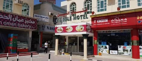 A hotel with a red and white facade, a visible entrance, and signage for a bakery and a maintenance company.