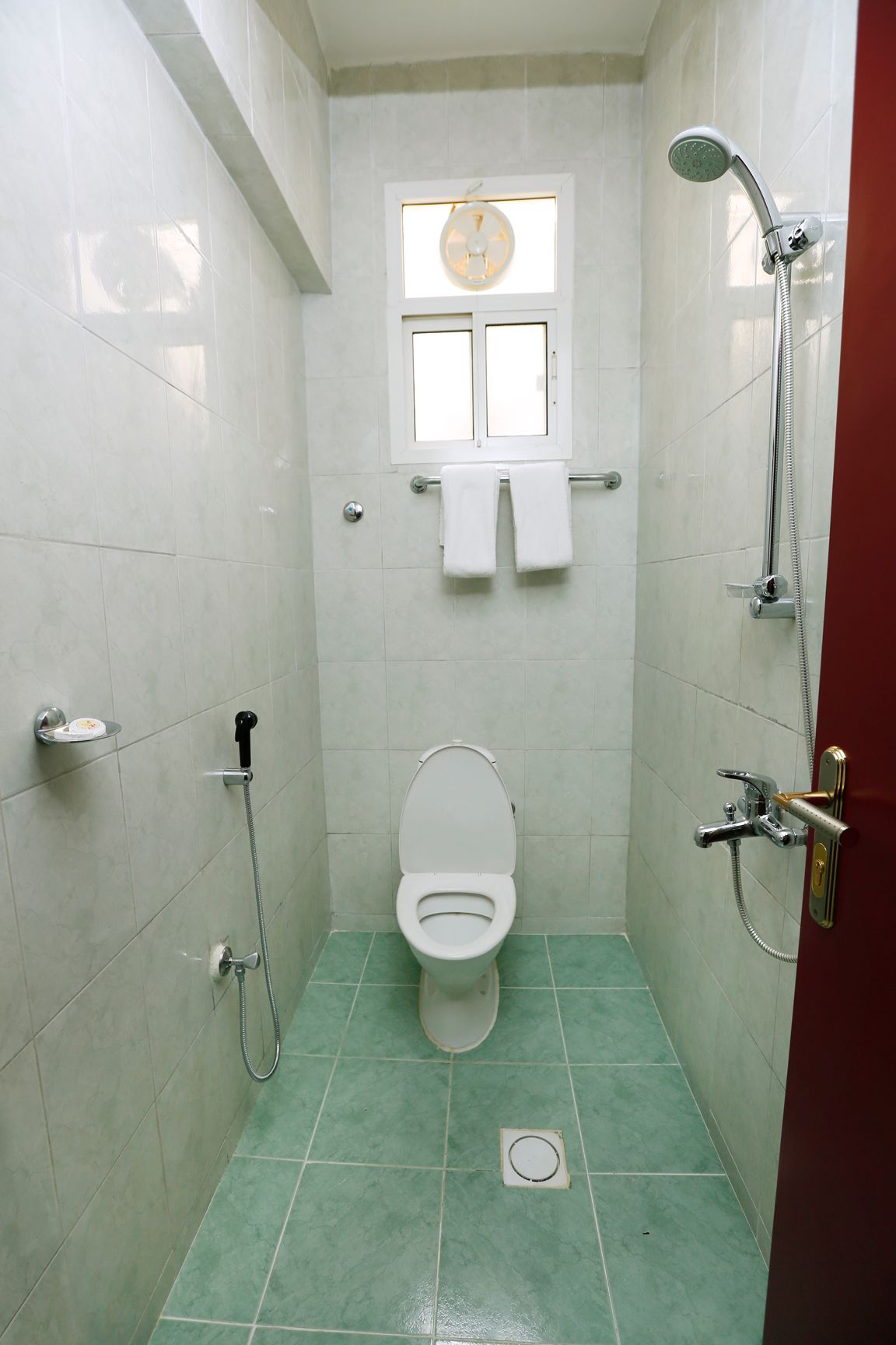 A small, tiled bathroom with a toilet, a shower, and a window above the toilet.