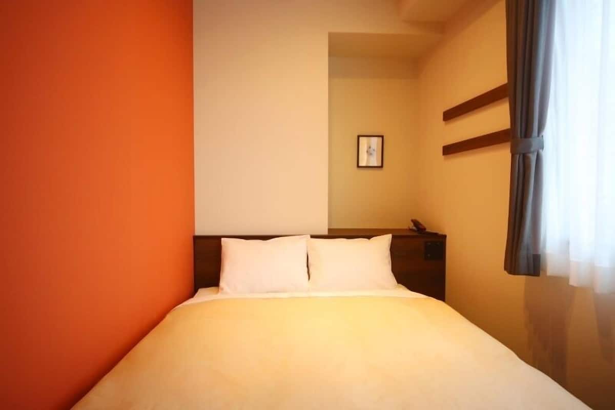 A hotel room with a bed, a nightstand, a framed picture on the wall, and a window with curtains.