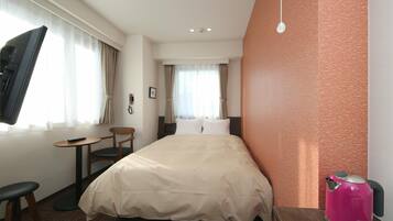 A hotel room with a bed, a desk, a chair, a television, and a kettle.