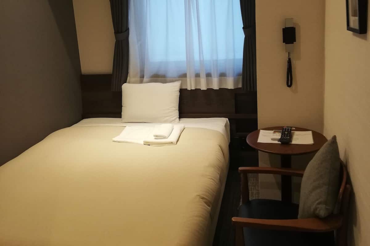 A hotel room with a large bed, a small table with a remote control, a chair, and a nightstand.