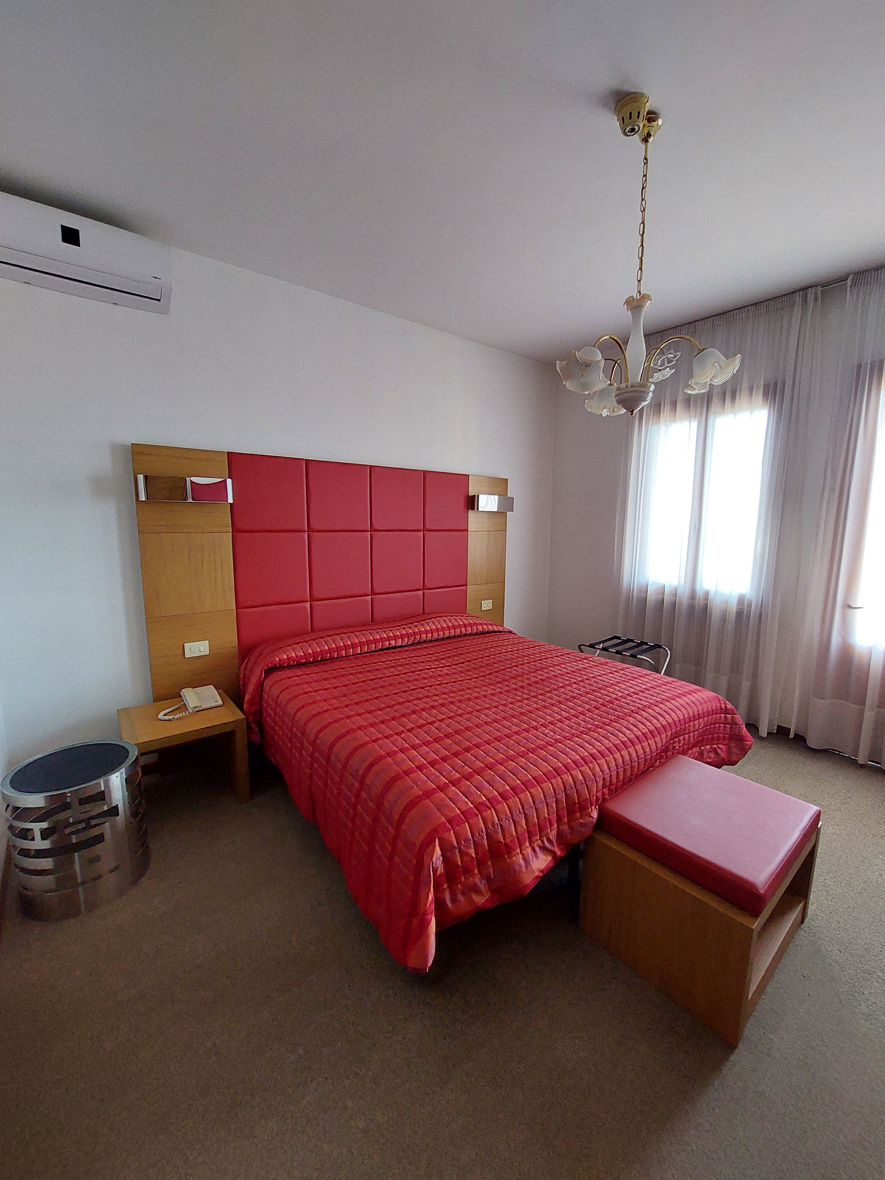 Un dormitorio con una cama grande, una mesita de noche, un cubo de basura y una ventana con cortinas.