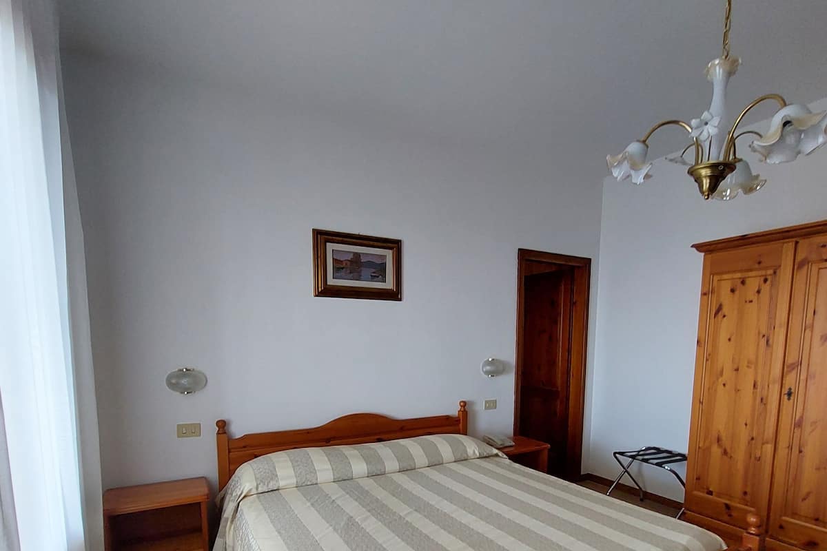 A bedroom with a wooden bed, a nightstand, a wardrobe, and a chandelier.