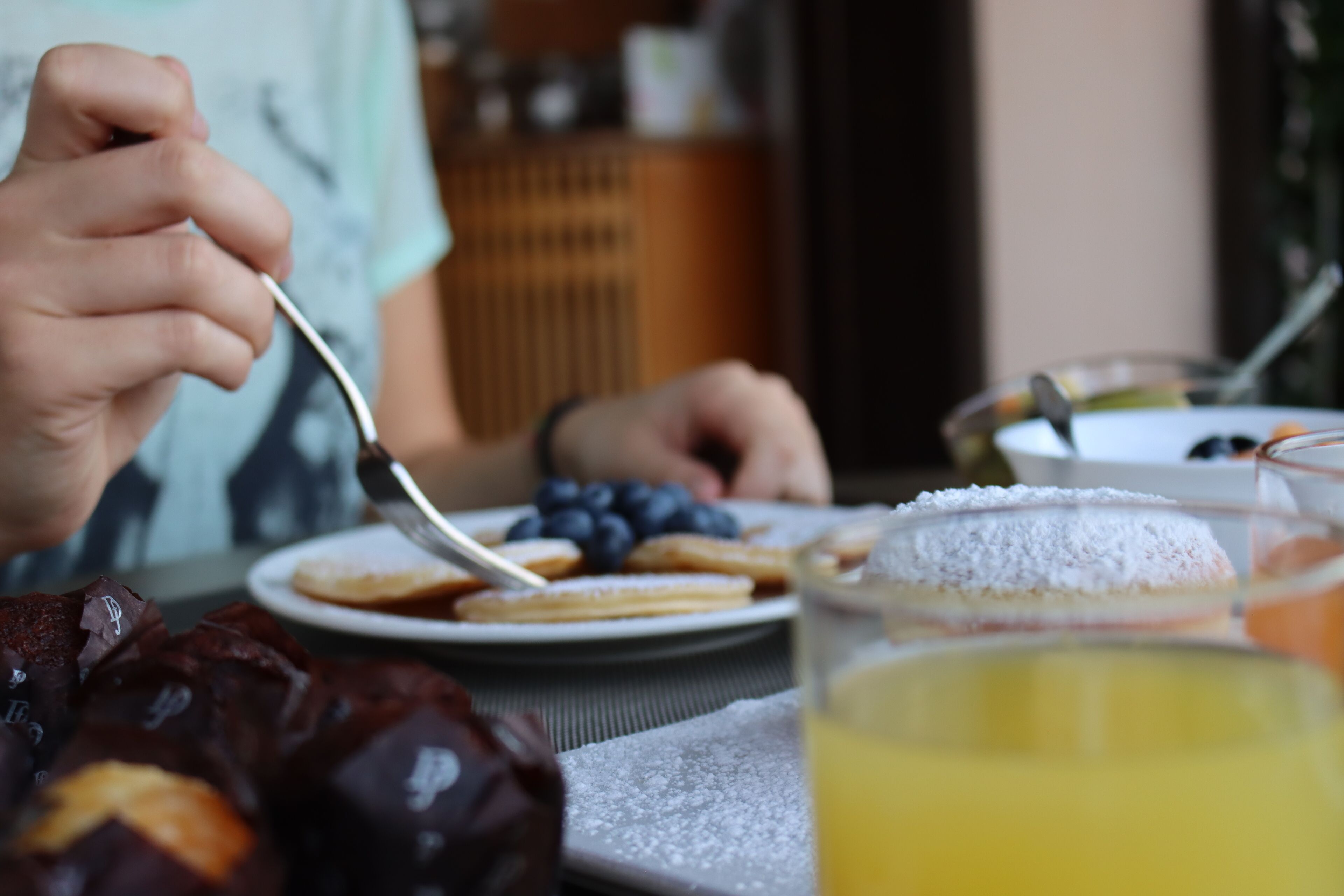 A dining table with a plate of food, a glass of juice, and a person eating.