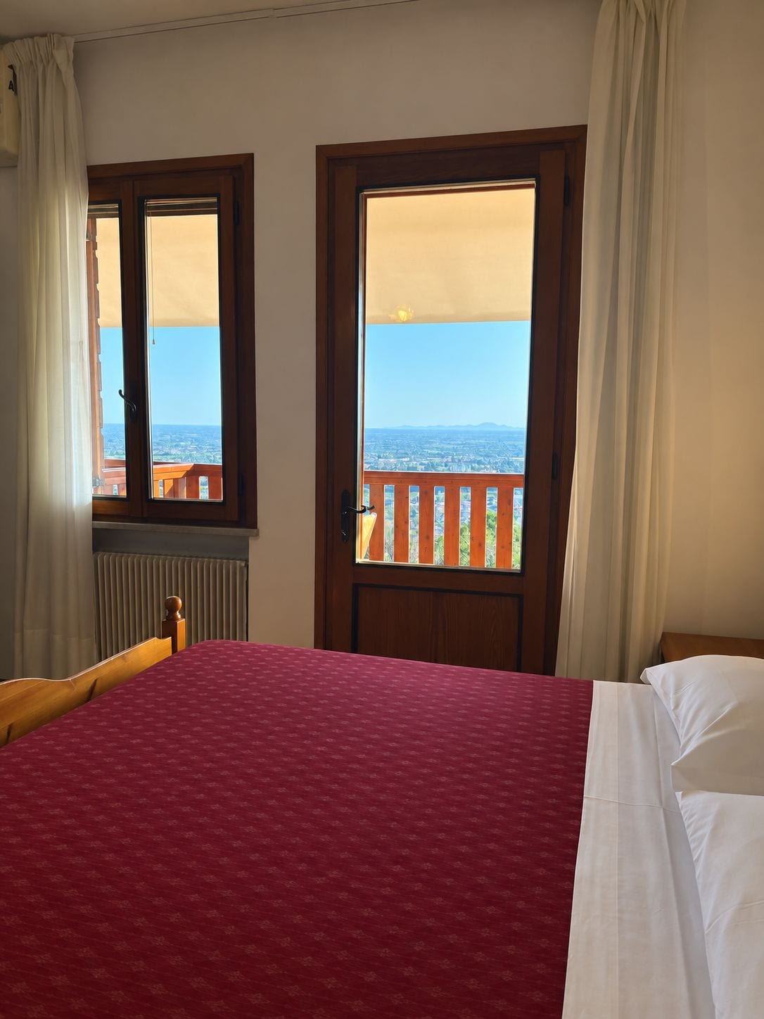 A bedroom with a bed, a window with a view of the sea, and a balcony with a railing.