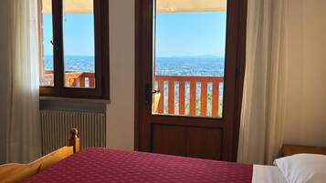 A bedroom with a bed, a window with a view of the sea, and a balcony with a railing.