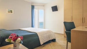 Une chambre d’hôtel avec un lit, un bureau, une chaise, une télévision et une fenêtre avec des rideaux.
