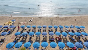 Une plage bordée de rangées de parasols bleus et de chaises longues, une étendue de sable et l’océan en toile de fond.