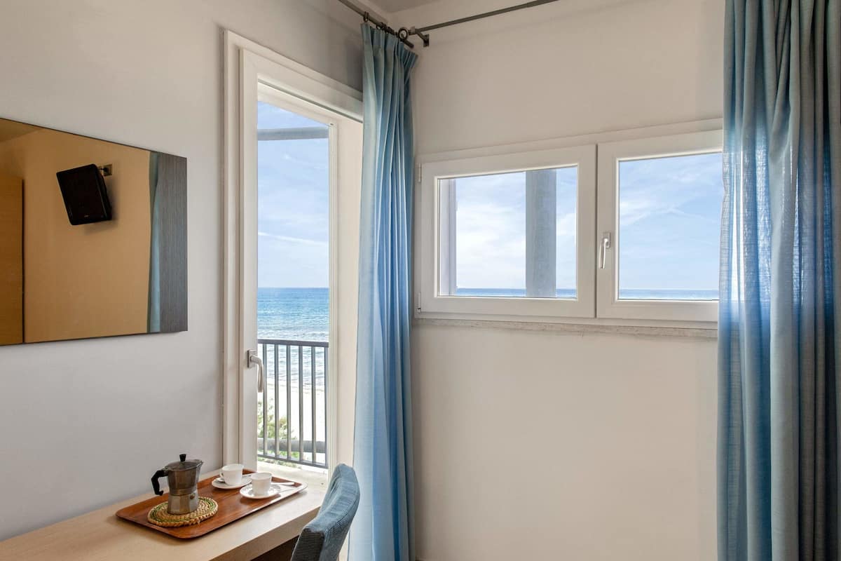 Una habitación con vista al mar, una mesa con cafetera y tazas, y un cuadro en la pared.