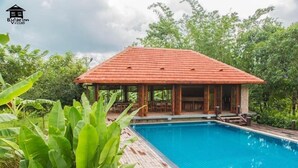 A poolside area with a wooden deck, a covered seating area, and lush greenery. - Bulaeinn Villas (Bago)