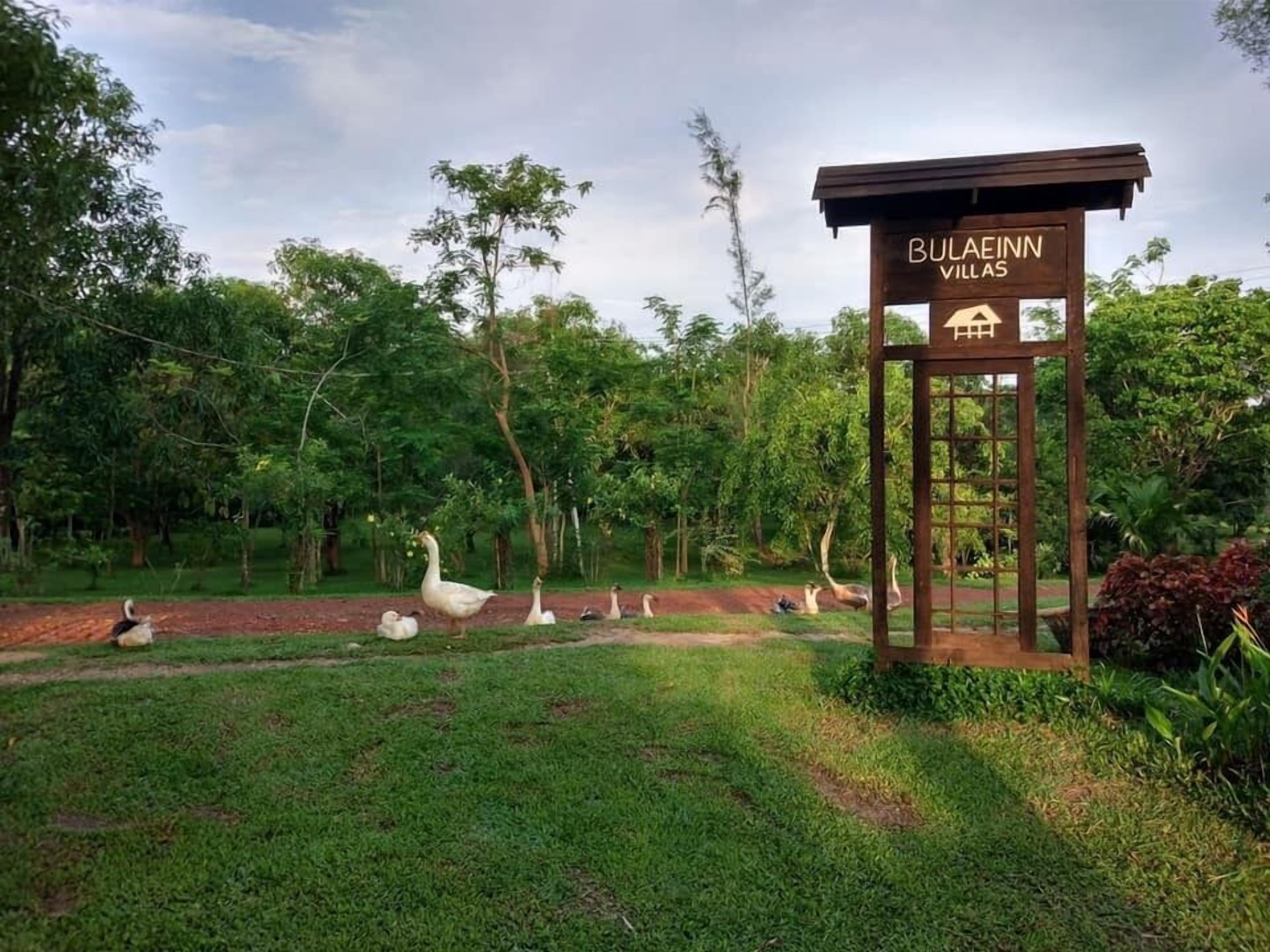 A sign for Bulacinn Villas with a view of a grassy area and trees.