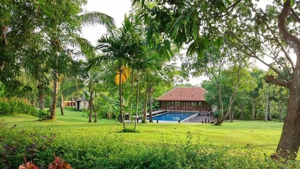 A pool area with a building in the background, surrounded by lush greenery and palm trees. - Bulaeinn Villas (Bago)