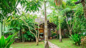 A lush garden with a wooden pathway leading to a traditional building with a tiled roof. - Bulaeinn Villas (Bago)