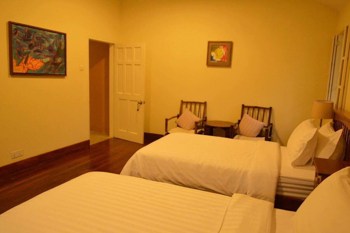 Habitación de hotel con dos camas, una mesita, dos sillas y una puerta.