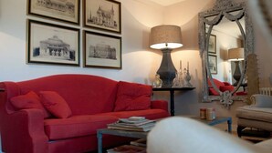 Een woonkamer met een rode bank, een lamp, een spiegel en lijstjes met foto's aan de muur.