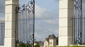 Een toegangshek met een ijzeren poort en witte kolommen.