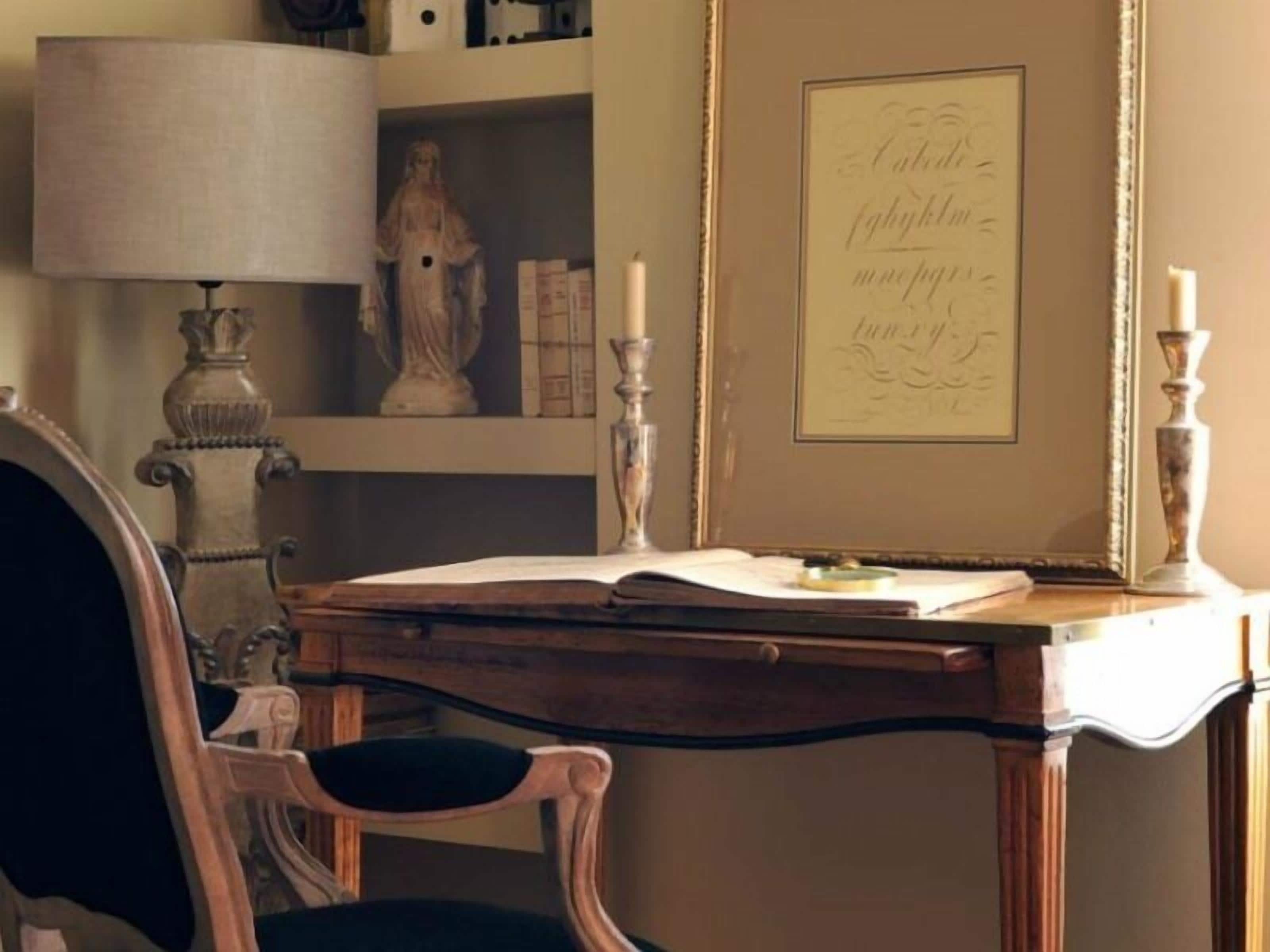A wooden desk with an open book, a lamp, and a framed quote on the wall.