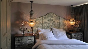 Een slaapkamer met een groot bed, twee nachtkastjes met decoratieve lampen, en een hoofdbord met een bloemenprint.