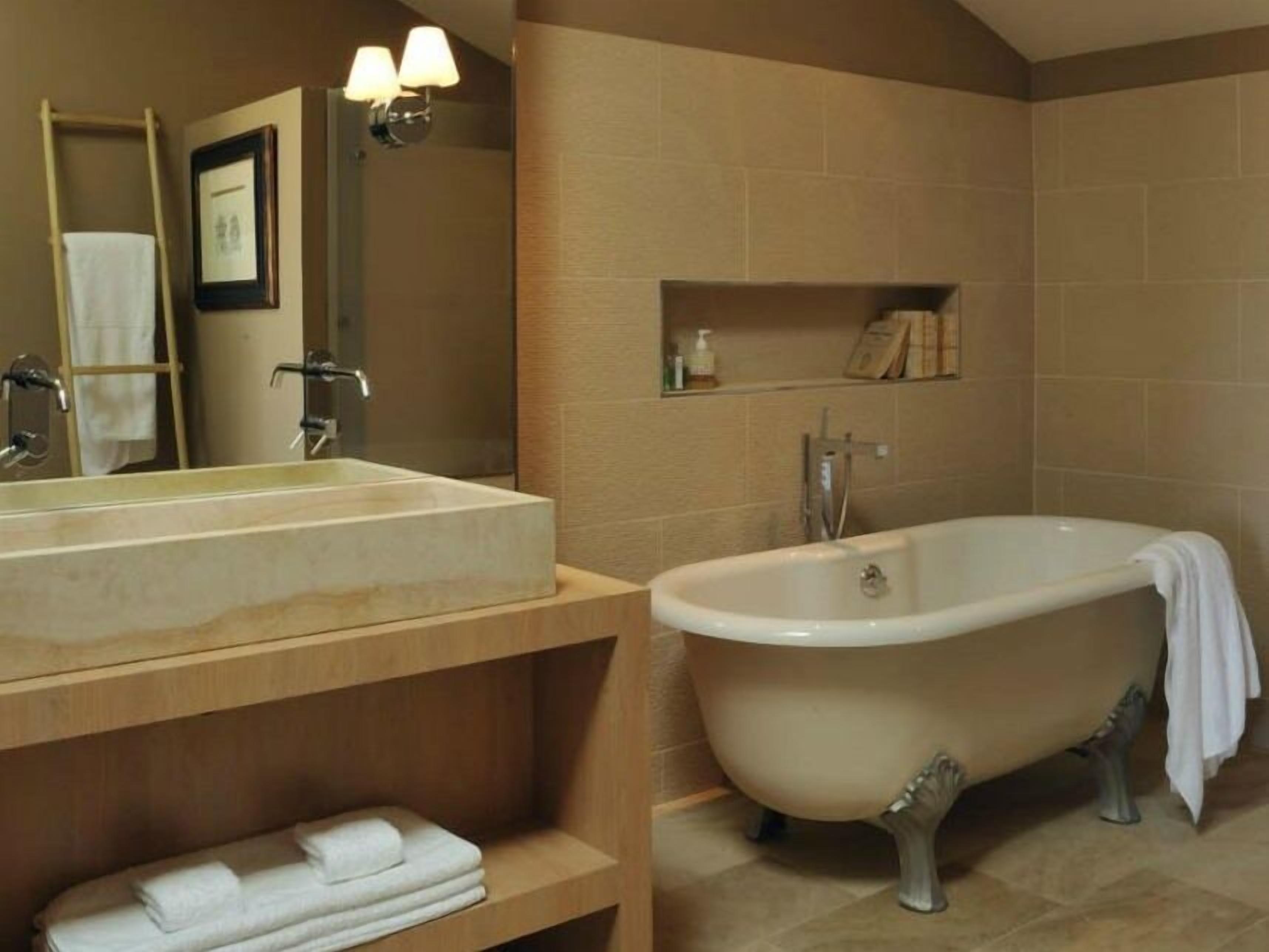 A bathroom with a freestanding bathtub, a large mirror, and a wooden vanity with a towel rack.