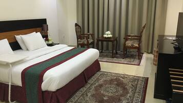 A hotel room with a bed, a desk, a chair, a TV, and a window with curtains.