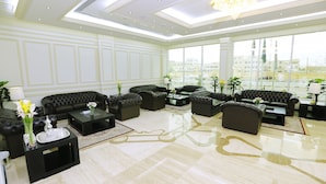Eine geräumige Lobby mit mehreren Ledersofas, einem zentralen Couchtisch und einem großen Fenster mit Blick auf die Stadt.