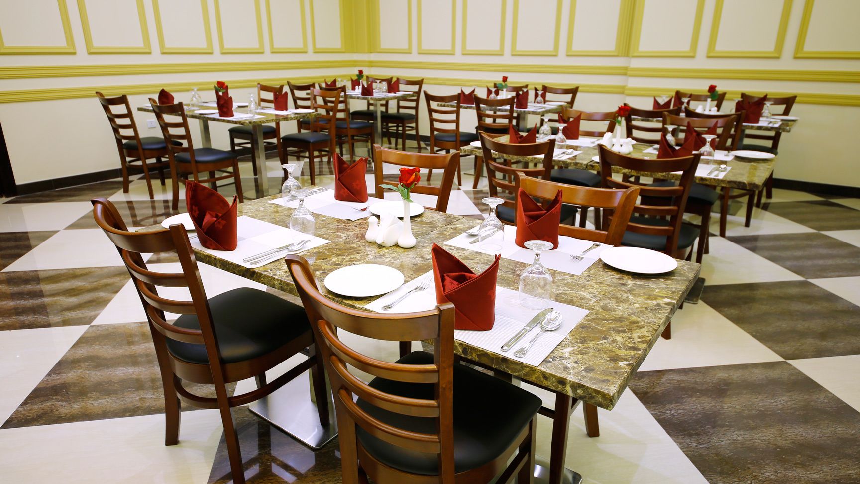 A dining area with round tables, each set with white plates, red napkins, and silverware.