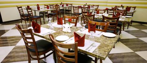A dining area with round tables, each set with white plates, red napkins, and silverware.