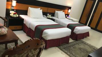 Ein Hotelzimmer mit zwei Einzelbetten, einem Nachttisch mit Lampe, einem kleinen Tisch mit Blumenvase, einem Sessel und einem Teppich.