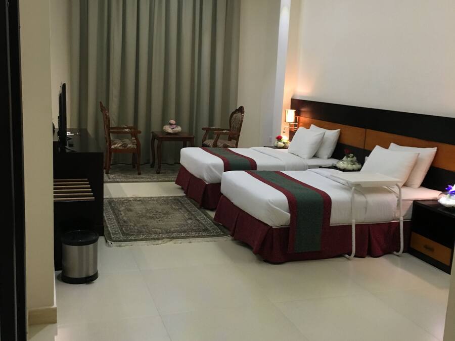 A hotel room with two beds, a desk, a chair, a small table, and a trash bin.