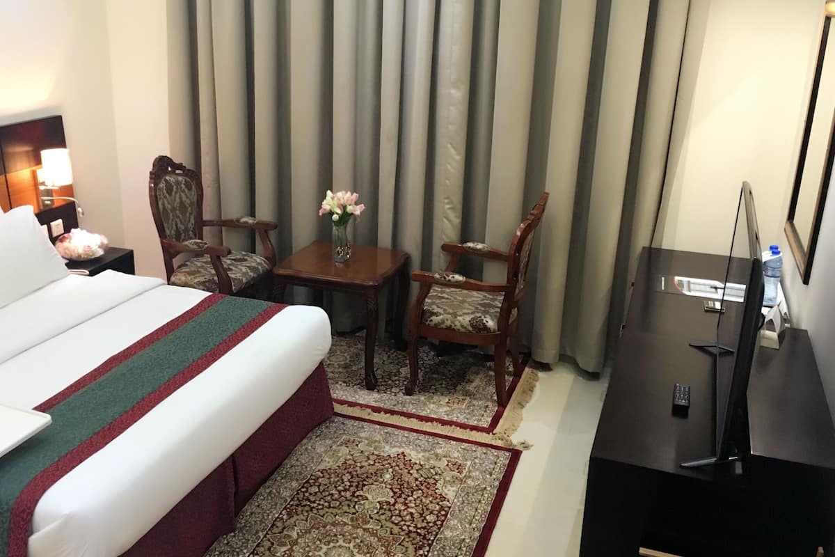 A hotel room with a large bed, a desk, a chair, a TV, and a window with curtains.