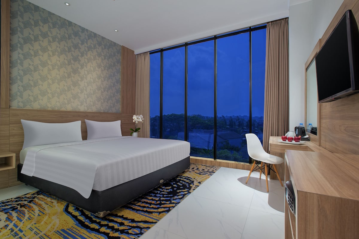 Una habitación de hotel moderna con una cama grande, un escritorio, una silla y un televisor.