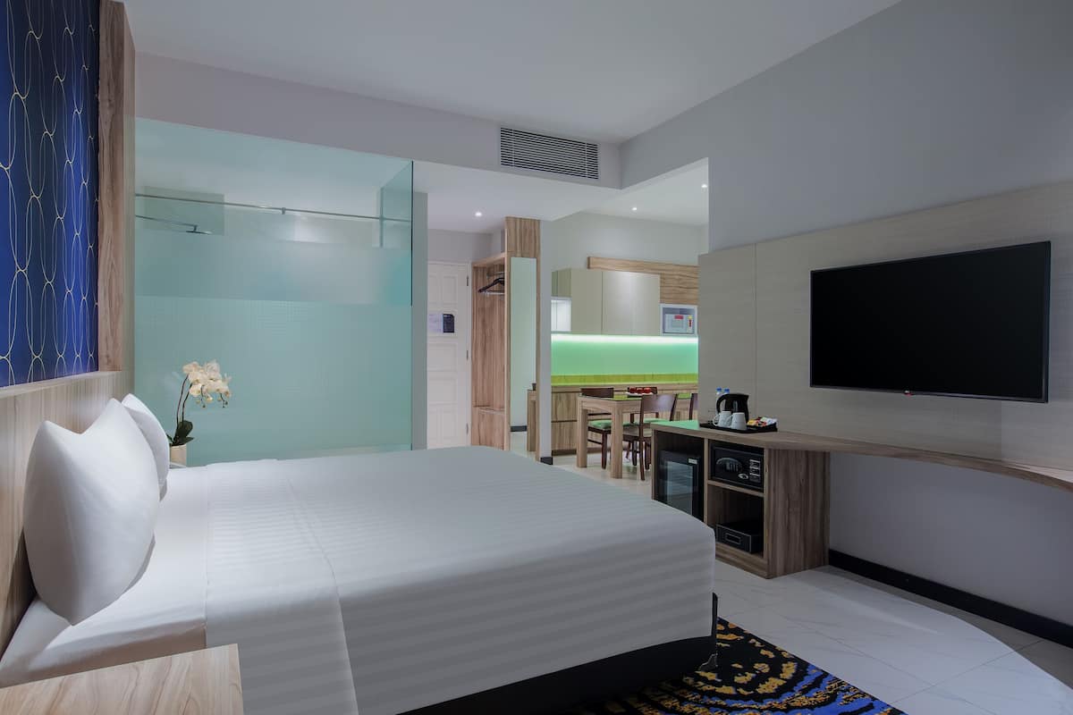Una habitación de hotel moderna con una cama grande, un televisor de pantalla plana, un escritorio con ordenador y una kitchenette pequeña.
