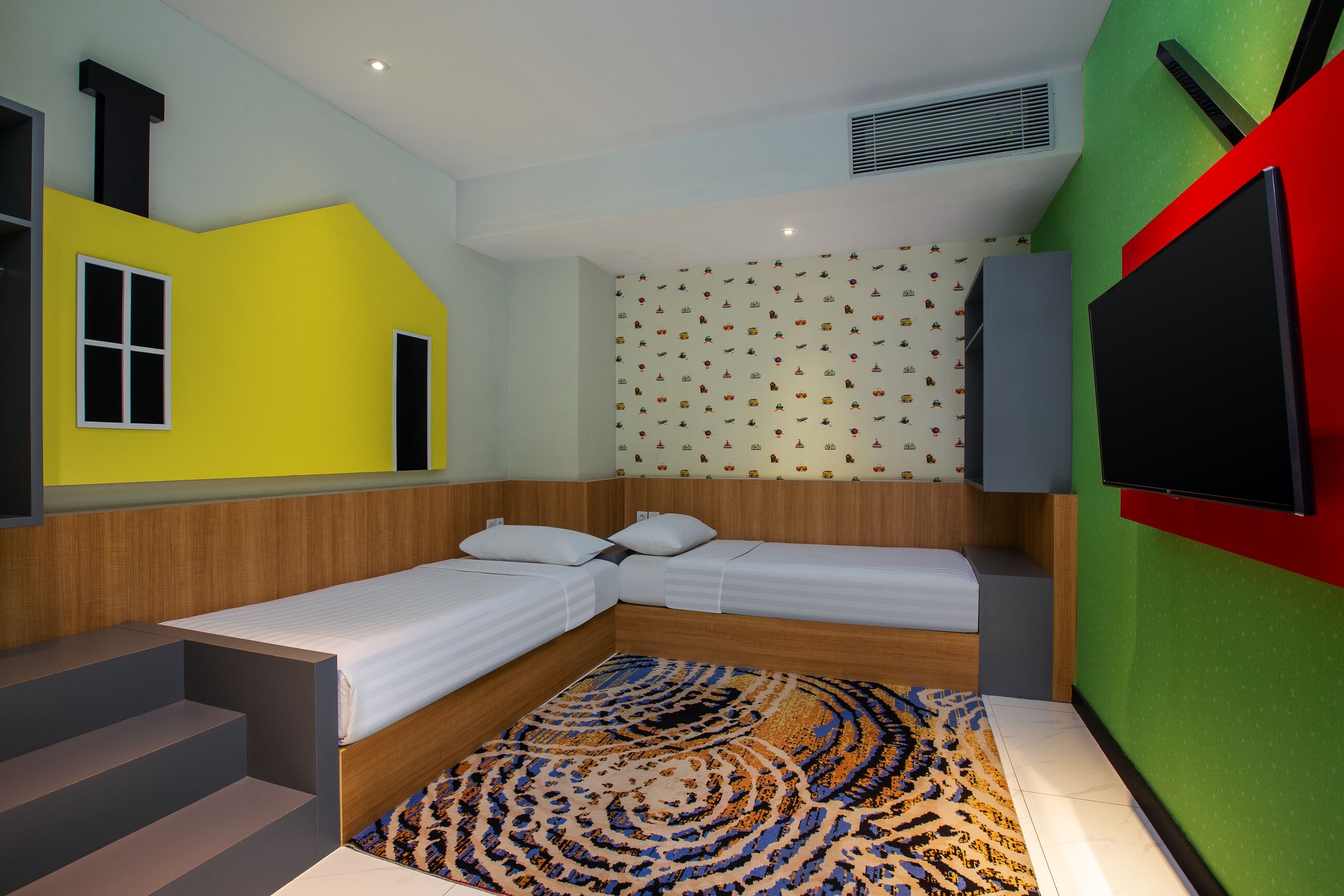 A room with two beds, a TV, and a patterned rug.