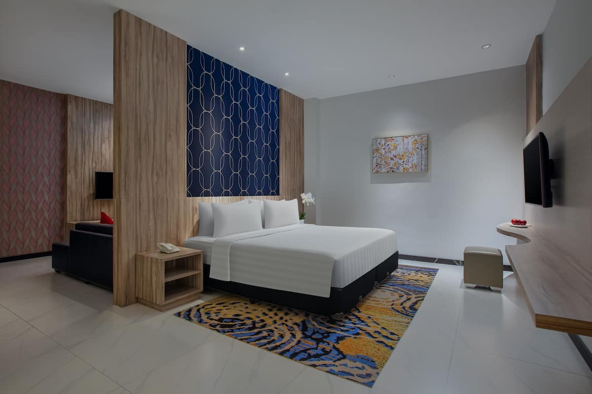 Habitación de hotel moderna con una cama grande, una mesita de noche de madera, un escritorio y una televisión.