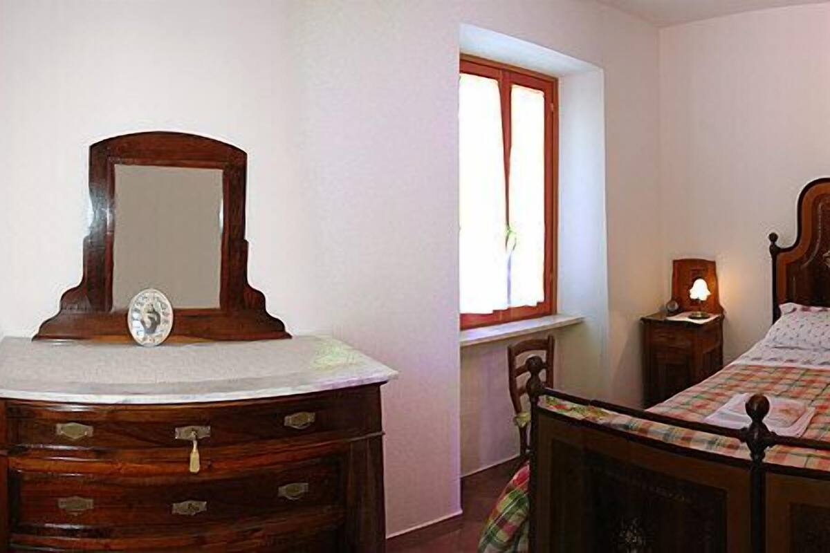 Une chambre à coucher avec un lit en bois, une table de chevet, une commode avec un miroir et une fenêtre.