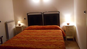 A bedroom with a bed, two bedside tables, a nightstand, a radiator, and a wall-mounted light fixture. - Agriturismo Monti Sibillini Camperato (Preci)