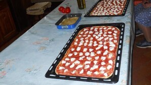 A kitchen with two pizza pans on a table, a bottle of olive oil, and a blue tray. - Agriturismo Monti Sibillini Camperato (Preci)