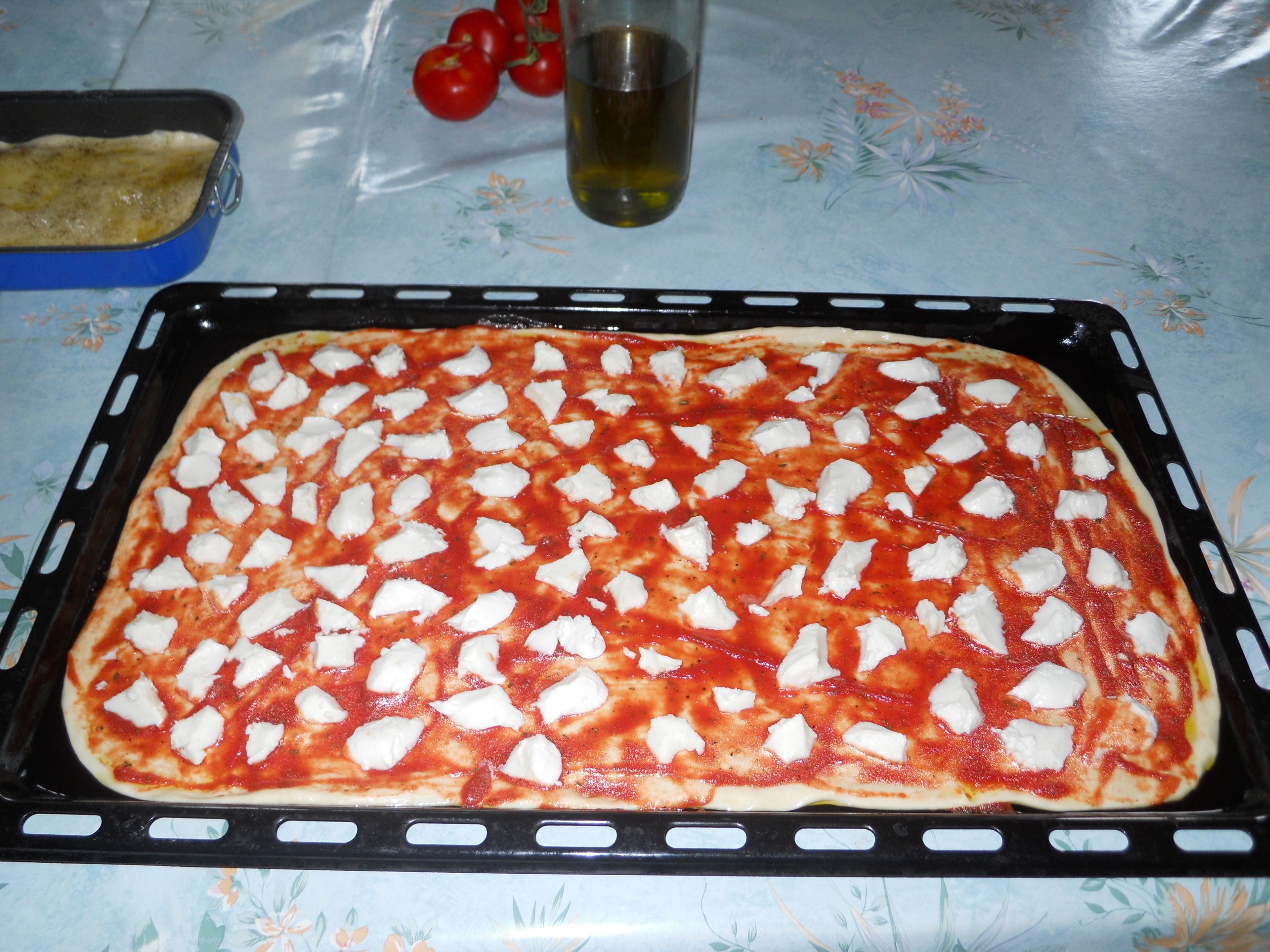 Une pizza sur une plaque de cuisson, garnie de sauce tomate et de fromage.