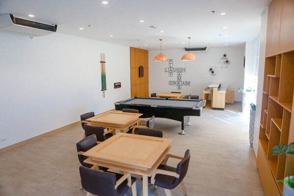 A room with a pool table, chairs, and a wooden cabinet.