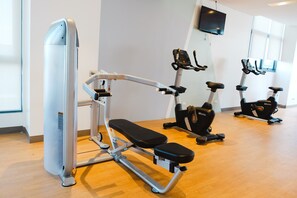 A gym with cardio machines, a TV mounted on the wall, and a wooden floor. - My Suits at Mactan Newton (Lapu-Lapu)