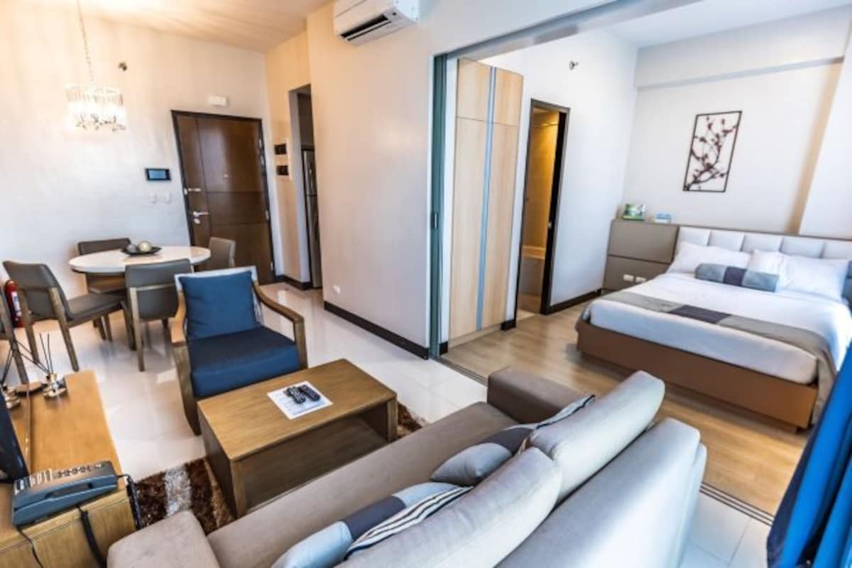 A modern hotel room with a sofa, a bed, a dining area, and a bathroom.