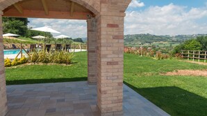An outdoor patio area with a brick archway, a pool, and a view of the countryside. - CasalFarano (Cupra Marittima)