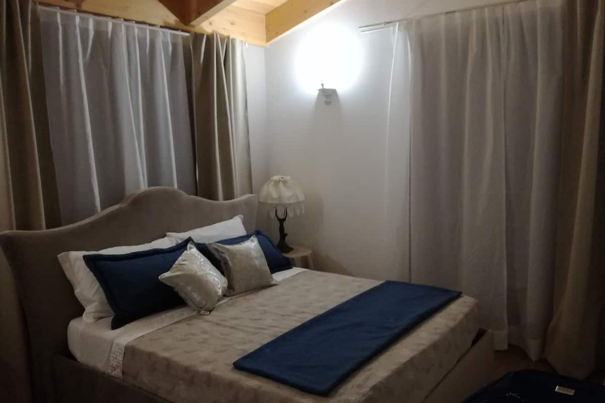 Un dormitorio con cama, cortinas, lámpara y maleta.