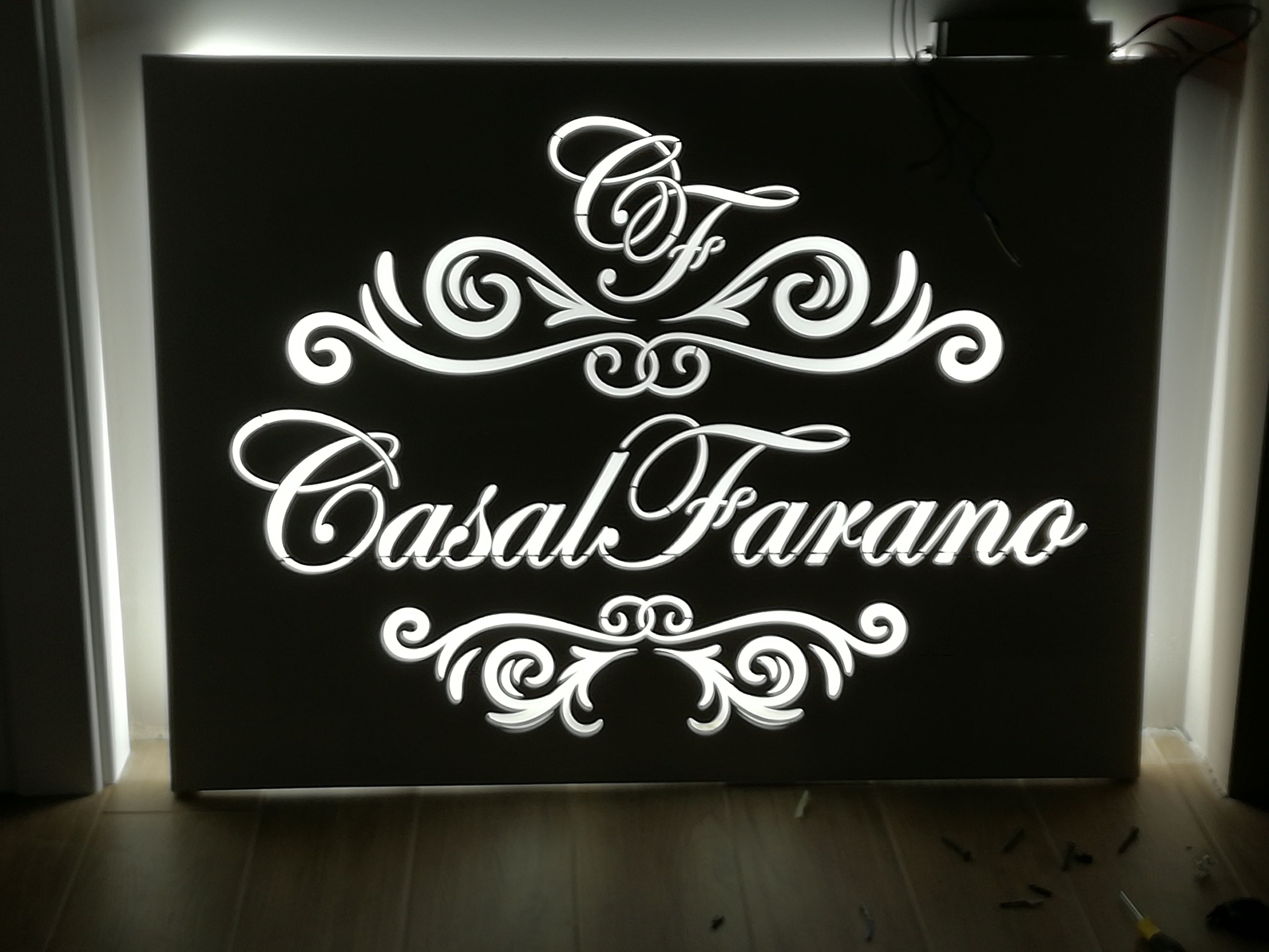 Uma placa preta com escrita decorativa branca e arabescos, com a inscrição 'Casal Farano'.