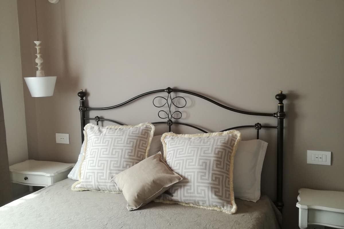 Una cama bien hecha con almohadones estampados, una mesita de noche y una lámpara colgante.