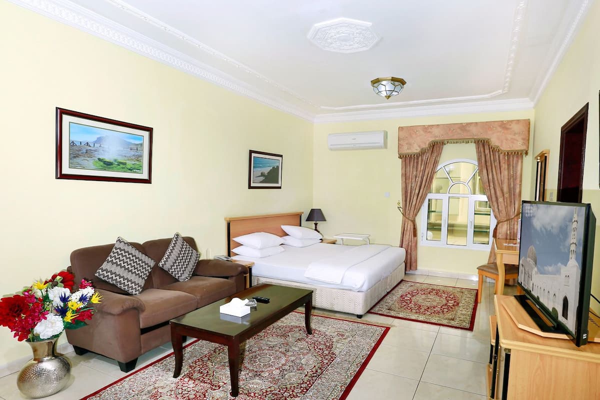 A hotel room with a bed, a sofa, a coffee table, and a TV.